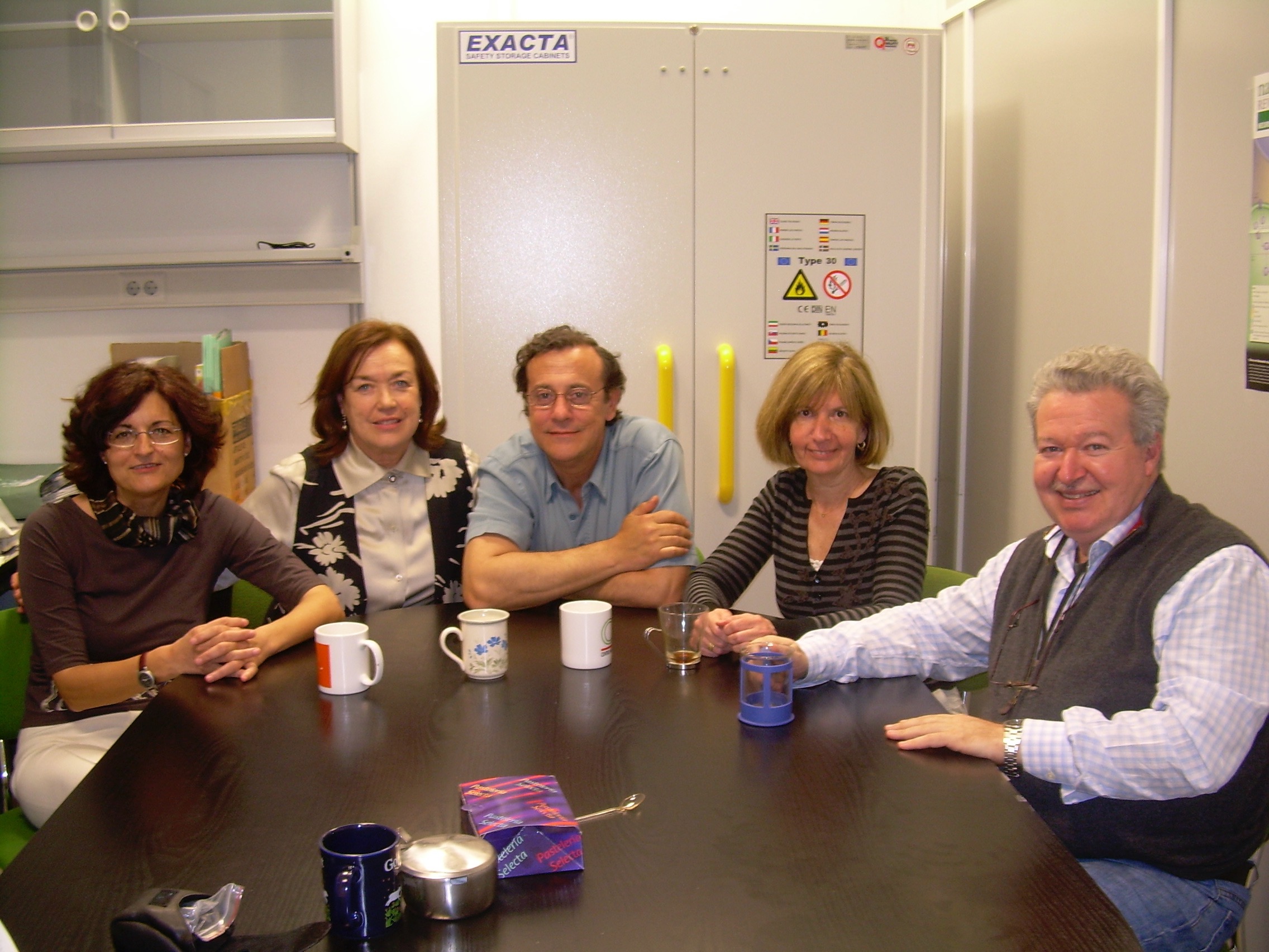 De izquierda a derecha:  María Luisa Martinez María del Carmen Partearroyo Pablo Hernández  Débora Krimer J. Bernardo Schvartzman  Reunidos alrededor de la “mesa negra” (traída del antiguo edificio de Velázquez), el grupo central de “Biología Molecular de los Cromosomas” compartiendo el café diario, un ritual que se repitió a lo largo de los años y que fortaleció una amistad que trascendió lo profesional.  Gathered around the “black table” (drawn from the old Velázquez building), the core group of “Molecula